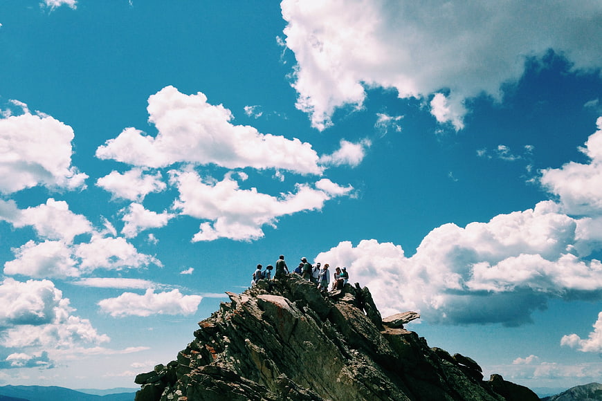 Group of hikers on rocky mountain peak under blue sky