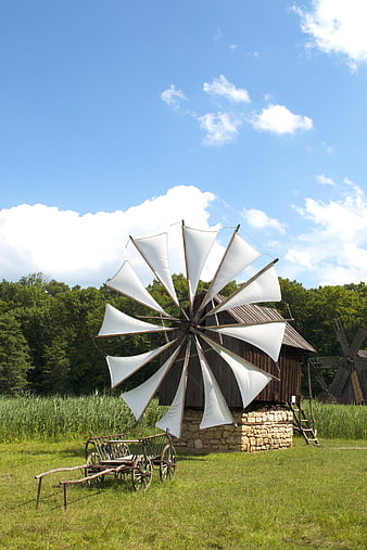 Traditional wooden windmill with white sails in a green field