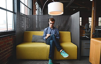 Young man writing on yellow sofa in modern office
