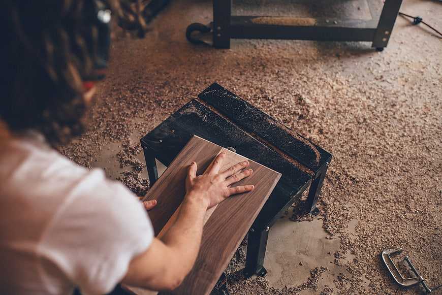 Carpenter sanding wood plank in workshop