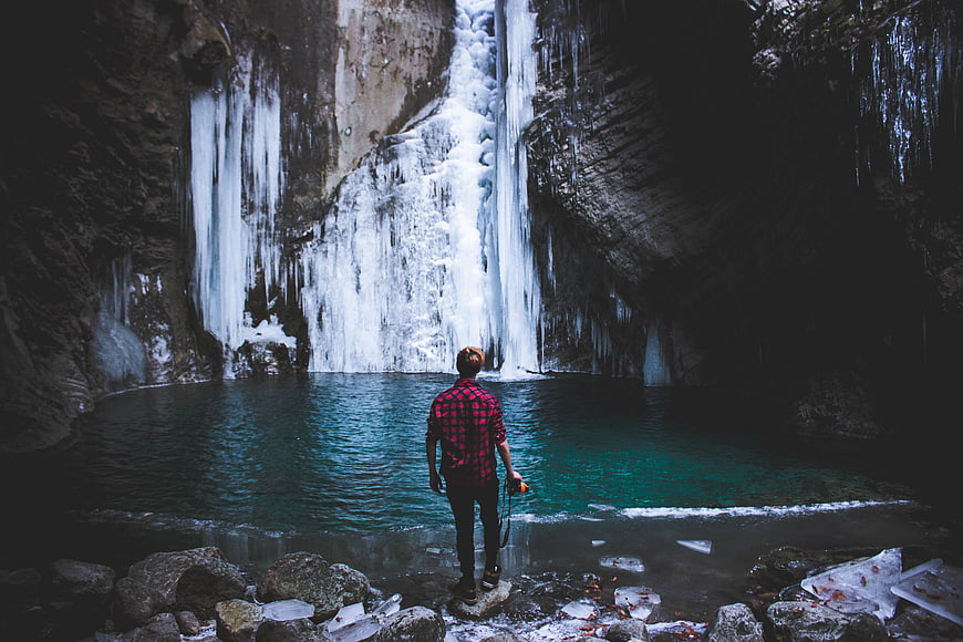 Man standing before frozen waterfall in winter canyon