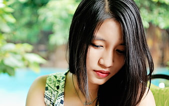 Close-up portrait of a young Asian woman looking down outdoors