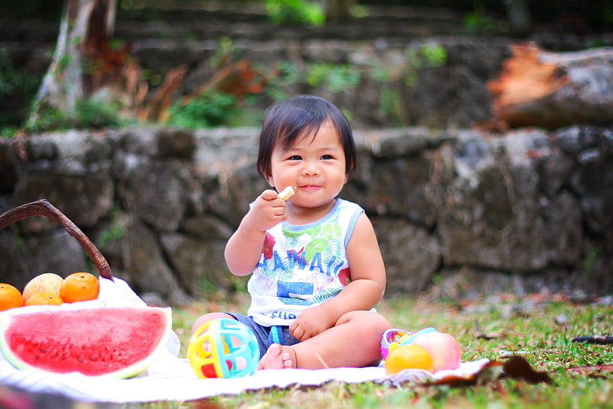 Happy toddler eating fruit at outdoor picnic
