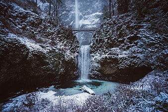 Snowy waterfall with bridge in winter forest landscape