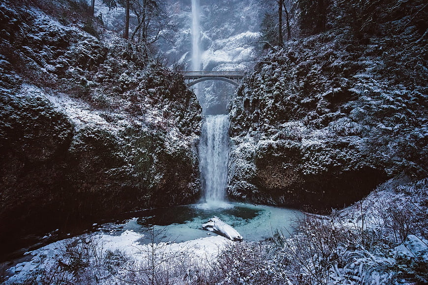Snowy waterfall with bridge in winter forest landscape