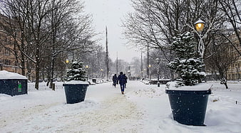 People Walking on Snowy City Path with Street Lamps