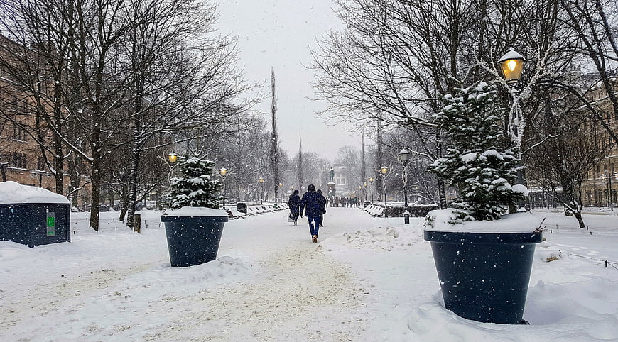 People Walking on Snowy City Path with Street Lamps