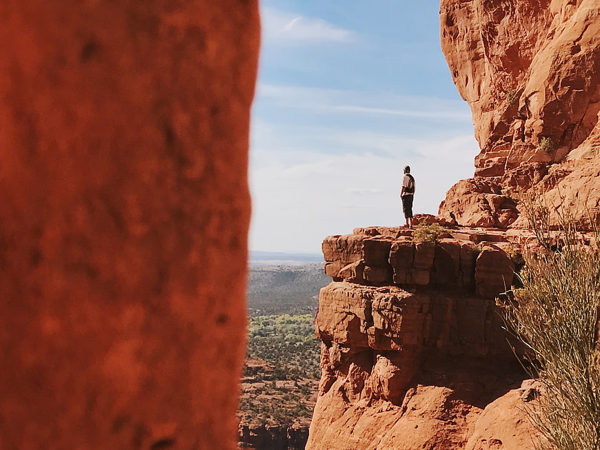 Man standing on red rock cliff edge looking at canyon view