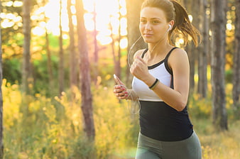Young woman jogging in forest with earphones and smartphone