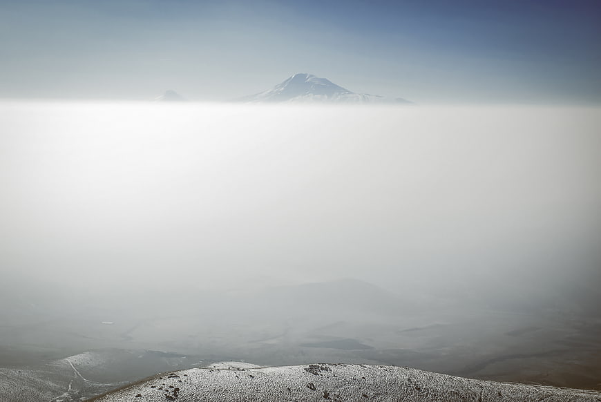 Snow-capped mountain peak rising above thick fog layer
