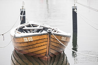 Snow-covered wooden boat docked in calm winter water