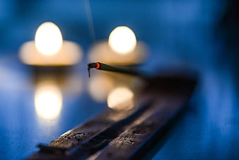 Burning incense stick with glowing ember and blurred candles