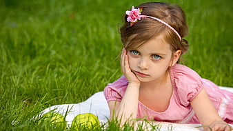 Sad little girl in pink dress lying on grass