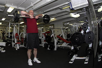 Senior man performing barbell shoulder press in commercial gym