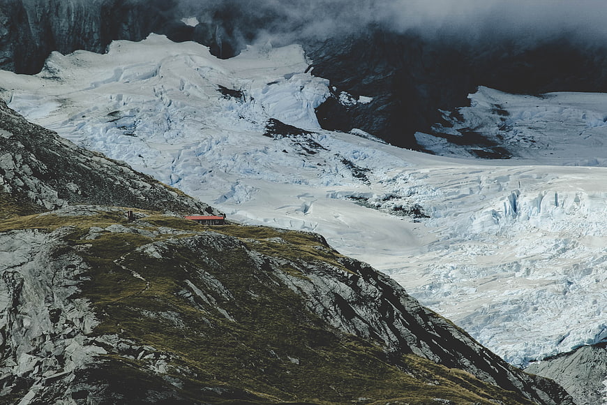 Alpine hut on rocky ridge overlooking massive glacier