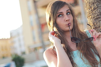 Young woman with sunglasses in mouth, outdoor portrait