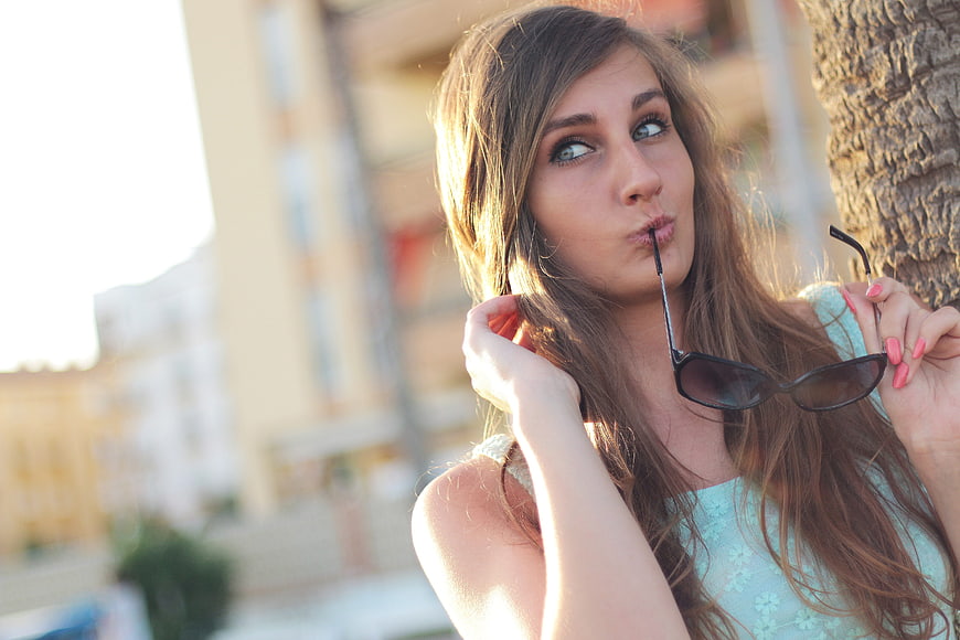 Young woman with sunglasses in mouth, outdoor portrait