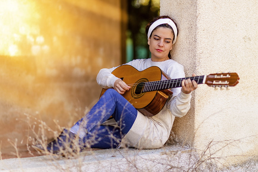 Woman playing acoustic guitar sitting against wall