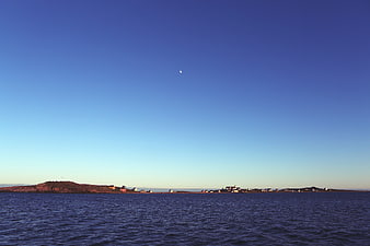 Coastal village landscape with crescent moon in blue sky