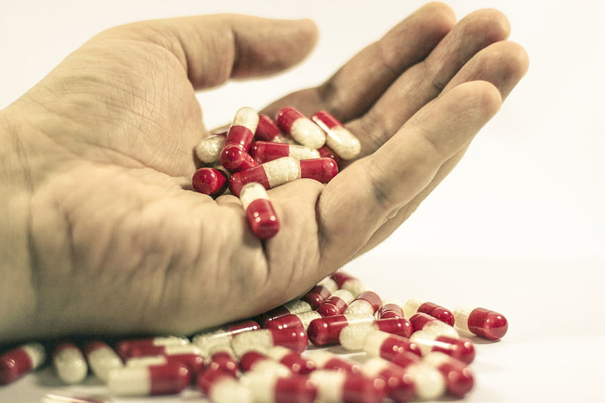 Hand holding red and white medical pills on white background