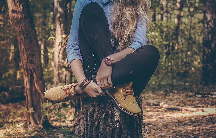 Woman tying shoelaces on tree stump in autumn forest