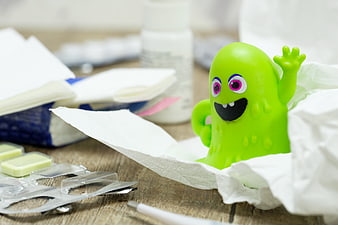 Green toy germ character surrounded by tissues and medicine on a wooden table