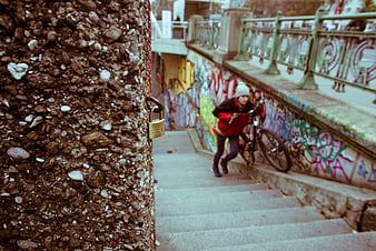 Woman pushing bicycle up graffiti-covered urban stairs