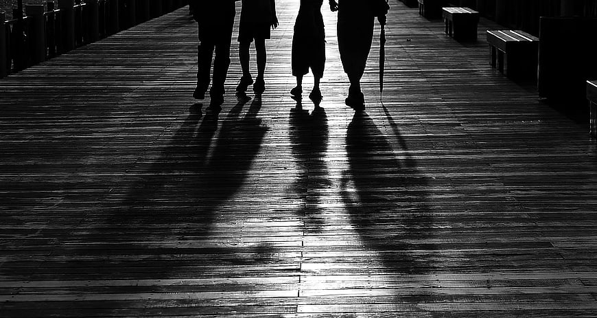 Silhouettes of four people walking on a wooden pier