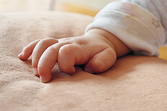 Close-up of baby hand resting on soft beige blanket