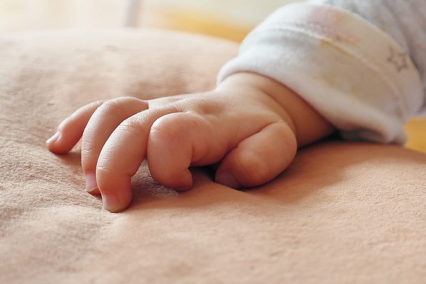 Close-up of baby hand resting on soft beige blanket