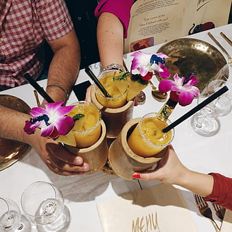 Hands clinking tropical cocktails with orchid garnish at restaurant