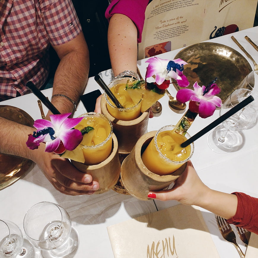 Hands clinking tropical cocktails with orchid garnish at restaurant