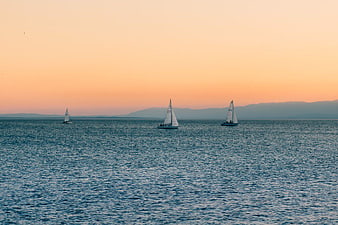 Sailboats on Ocean at Sunset with Distant Mountains
