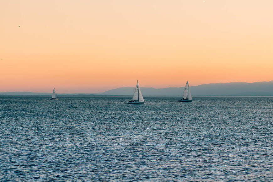 Sailboats on Ocean at Sunset with Distant Mountains