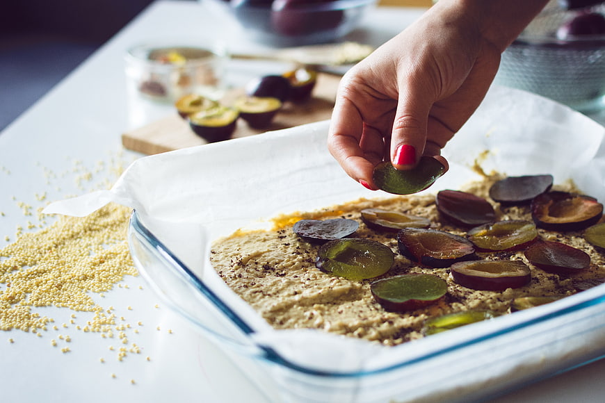 Hand placing plum slices on batter in baking dish
