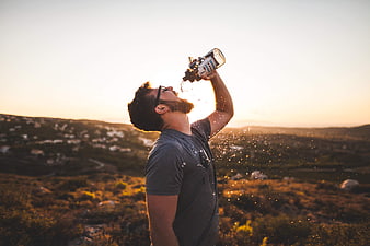 Man drinking water from bottle on mountain at sunset