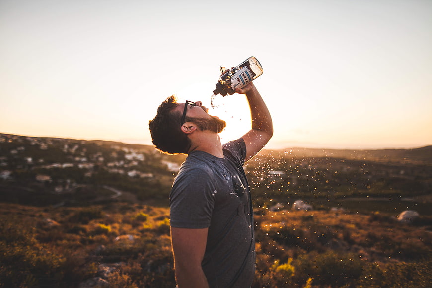 Man drinking water from bottle on mountain at sunset