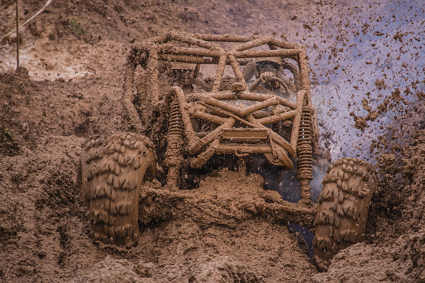 Muddy off-road buggy splashing through deep mud pit