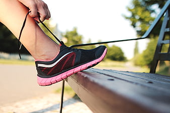 Woman tying pink and black running shoe on park bench
