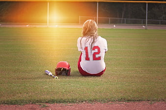 Teenage softball player sitting alone on field at sunset