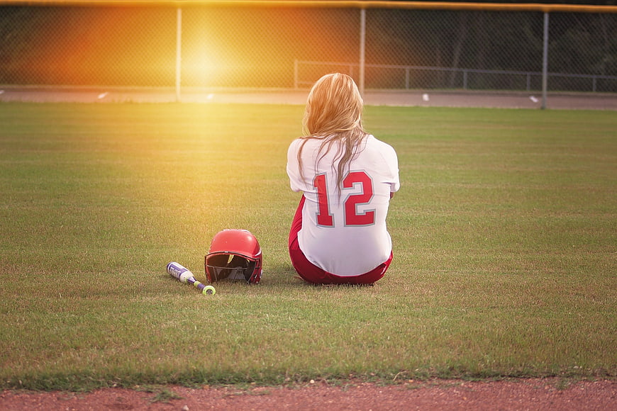 Teenage softball player sitting alone on field at sunset