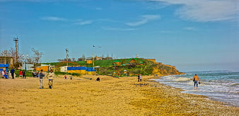 Wide panoramic view of a sunny beach with people and cliffs