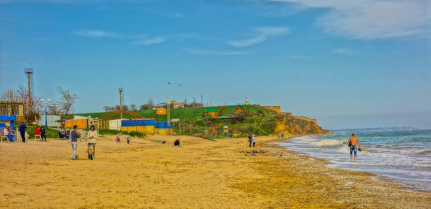 Wide panoramic view of a sunny beach with people and cliffs