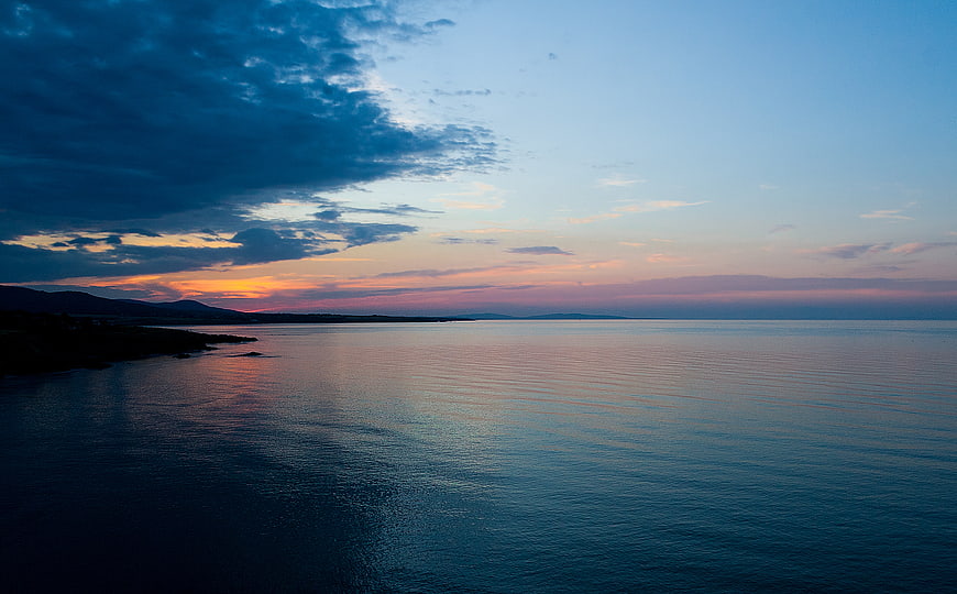 Serene Sunset Over Calm Ocean with Distant Mountains