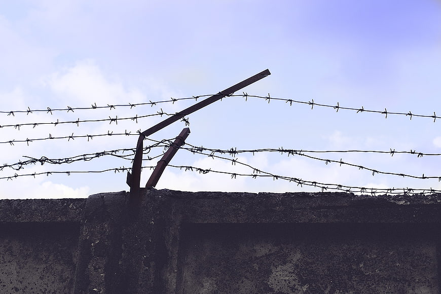 Barbed wire fence on concrete wall against blue sky