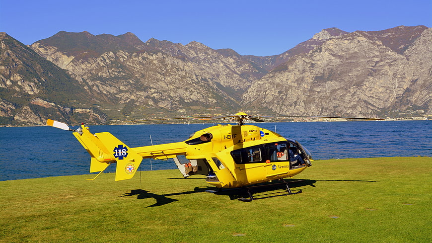 Yellow emergency helicopter on grassy landing pad near lake and mountains