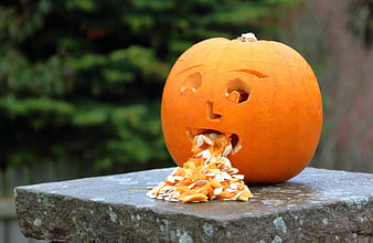 Carved Halloween Pumpkin Vomiting Seeds on Stone Surface