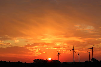 Silhouette of Wind Turbines Against Vibrant Orange Sunset Sky