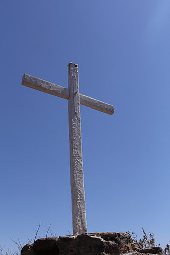 White wooden cross on rocky hill against blue sky
