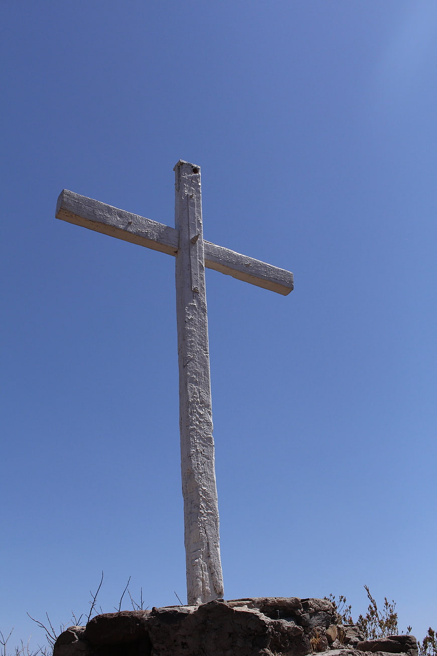 White wooden cross on rocky hill against blue sky